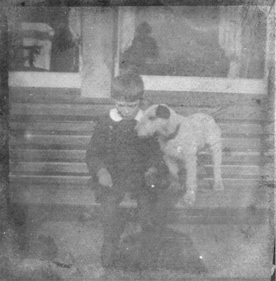 A poor picture of a boy sitting on a bench with his pet terrier
