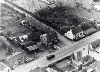1950s aerial photograph of the High Street and Barkestone Lane/Albert Street junction. On the south side can be seen Eric George's Butcher's shop; the old Post Office; the offices of W.J. Roberts and the white cottage, 'The Rosary'. On the north side in the foreground: Vine House and the Gas Showrooms