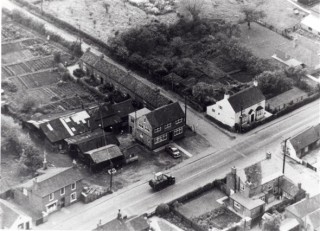 BLHS0012_MH3 1950s aerial photograph of the High Street and Barkestone Lane/Albert Street junction. On the south side can be seen Eric George's Butcher's shop; the old Post Office; the offices of W.J. Roberts and the white cottage, 'The Rosary'. On the north side in the foreground: Vine House and the Gas Showrooms