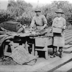 Picture 8. As the brickmaker gathers clay for the next brick, the boy takes the filled mould away.