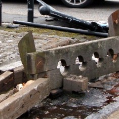 Demolished road sign, broken bollards and railing, stocks knocked off base and whipping post flattened