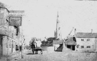Behind the cross on the left, the butcher's shop, now a two story building, but still a butcher's. On the right John Sutton's shop