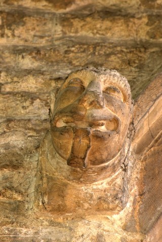 P1050468 This face is on the west-facing side of the wall separating the south transept from the aisle. A man's face, gazing upwards reverentially, his mouth gaping, and a strange straplike feature on his chin. What is it intended to show?