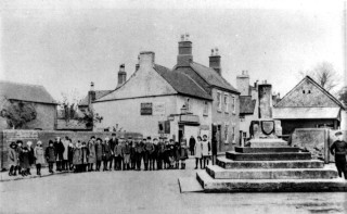 Bottesford School Children at the cross. Behind them, The Old White House, then Samuel's shop. 1920s.