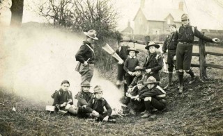 Bottesford Scouts camp fire c 1912. Standing left - Charles Calcraft; seated left of fire, L to R - unknown, Sydney Taylor, Arthur Taylor; standing right of fire L to R - Edgar Culpin?, Bill Cooper, Wilf/Harry? Challands; seated right of fire, L to R - Bob Sutton, Frank Sutton?, unknown; standing rear by fence: unknown, Harry Lane.