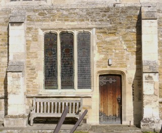 Exterior of the chancel showing traces of dog-tooth ornament and the line of an early arch embedded in the masonry above the more modern doorway.