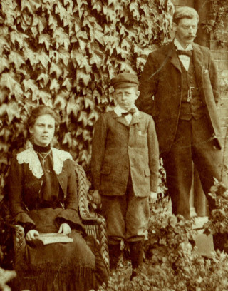 Thought to be Wilfred (rather than Victor) Barrand, aged c.10, between his aunt Mary Elizabeth Collet and uncle Victor Collet, outside the School House, c.1910. | From the Webster private collection.