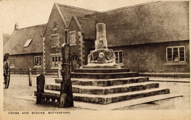 Postcard of the Market Cross and Stocks, with the village school behind.