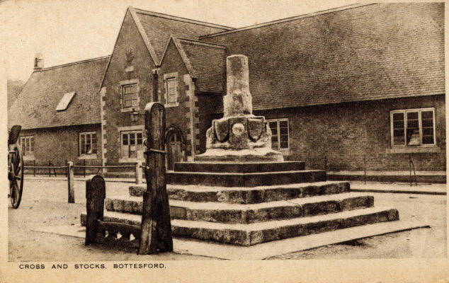 BOT025_032_MS old cross 2 Postcard of the Market Cross and Stocks, with the village school behind.