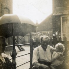 BOT177_013 Marston album1 13 #2 This family scene appears to be at the rear of the Marston's home on Queen Street. To left is probably the end of the Queen St mill buildings, and in the background is Queen Street and part of Tappins' cottage. Thw people are probably Frank Marston holding infant Daphne, and an unidentified woman holding an umbrella at the left edge of the picture. | Janet Dammes