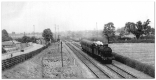 Bottesford for Belvoir - slide 30 The 'Joint' line in the 1950s, the view looking northwards from the approach bridge on Nottingham Road, Bottesford. On the left is the entrance to the WW2 Army Camp, on the right is the original Orston Lane (now Bowbridge Lane) as it reaches the level crossing with the railway line. Beyond the crossing Bottesford South signal box is visible, and on the horizon is the embankment of the old Ambergte railway and bridge beneath which the Joint line ran. | From the collection of the late Mr Ken Greasley.