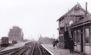 Bottesford for Belvoir - slide 40 Bottesford station looking westwards. A family is approaching the track-level pedestrian crossing to reach the southern platform and exit to Station Road. In the distance is the gate-keeper's cottage on the old road to Normanton and Allington, and in the far distance is the keeper's cottage on the level crossing on Normanton Road. | From an old postcard