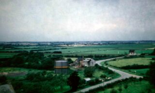 Bottesford for Belvoir - slide 44a Taken by Police Sgt Artur Bradshaw during a visit to the top of Bottesford St Mary's tower c.1950. Normanton Lane crosses the railway at the manually operated level crossing after passing the village's small gas works. A goods trains is approaching heading eastwards. | Donated by Mr Michael Bradshaw