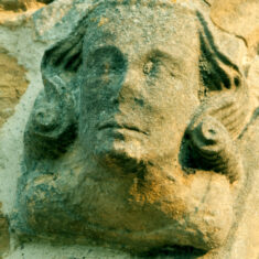 One of two heads, probably both of men despite the long hair (perhaps a 17th Century hair style), at the ends of the hood mould of the north transept window, seeming to be stuck on rather than an integral part of the structure, and thus later than the Perpendicular window itself. | Neil Fortey
