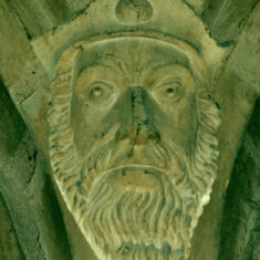 Above the southern side of the nave are the heads of two bearded men. This one appears to be a king wearing a cap rather than a crown, with an oval jewel or badge attached at the front. In neither are the eyes painted black, though it appears that the pupils have been carved so that they stand out (or are they scooped back?) and may have black highlights positioned to create the appearance of a gaze directed upwards. | Neil Fortey