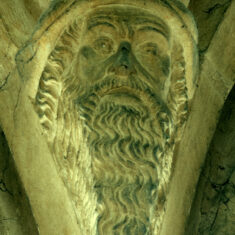 Above the southern side of the nave are the heads of two bearded men. This one appears to be a prophet (left), the other may be a king wearing a cap rather than a crown, with an oval jewel or badge attached at the front. In neither are the eyes painted black, though it appears that the pupils have been carved so that they stand out (or are they scooped back?) and may have black highlights positioned to create the appearance of a gaze directed upwards. | Neil Fortey