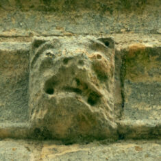 P1050508_05 One of the six small grotesque faces carved in the stones forming the frieze below the parapet of the tower.