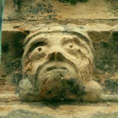 P1050511_05 One of the six small grotesque faces carved in the stones forming the frieze below the parapet of the tower.