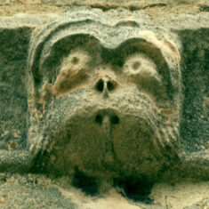 P1050514_06 One of the six small grotesque faces carved in the stones forming the frieze below the parapet of the tower.