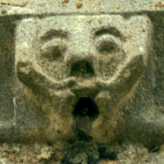 P1050525_06 One of the six small grotesque faces carved in the stones forming the frieze below the parapet of the tower.
