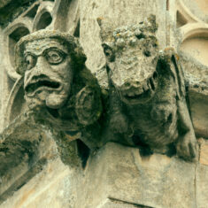 One of two views of the upper carving at the eastern end of the northern side of the clerestory, depicting a double figure, a man, apparently holding a sword in his right hand and a small, circular shield or drum in his left, accompanied by a winged dragon-like creature bearing its fearsome teeth. The man, with a strangely bulbous chin, looks anxious, but the dragon appears to be smiling. In Medieval theology the Devil was likened to a dragon because he was the worst of all serpents. This carving can be interpreted as showing a sinner who seems to have been ensnared by the Dragon/Devil. | Neil Fortey