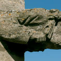 Two figures jut out one above the other on the eastern corner of the southern side of the clerestory. This, the lower one, is a bearded man wearing a cloth head-dress, not a king, but his dignified, bearded face and garments suggest a prominent person, perhaps a judge or a nobleman.  | Neil Fortey
